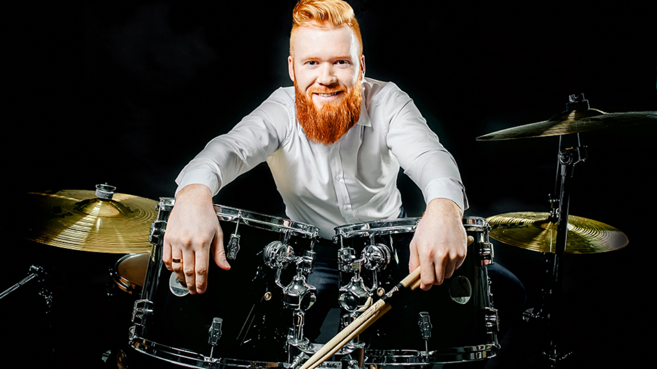 Portrait of a red-haired emotional man playing drums and cymbals and holding a stick. isolated on a dark background