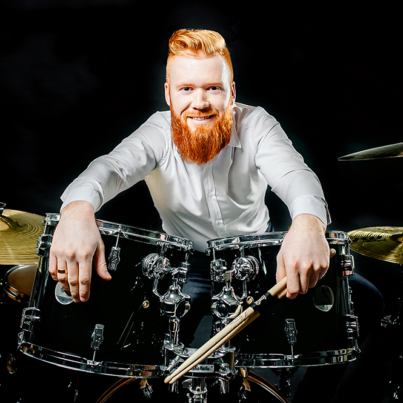 Portrait of a red-haired emotional man playing drums and cymbals and holding a stick. isolated on a dark background