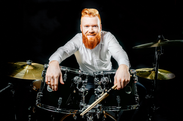 Portrait of a red-haired emotional man playing drums and cymbals and holding a stick. isolated on a dark background