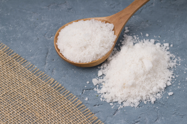 Crystals of large sea salt in a wooden spoon  on concrete background