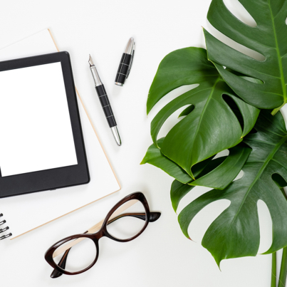 Flat lay tropical jungle Monstera leaves, paper notebook, e-book reader, glasses on white background. Top view feminine diary, stationery and electronic device on home office desk.